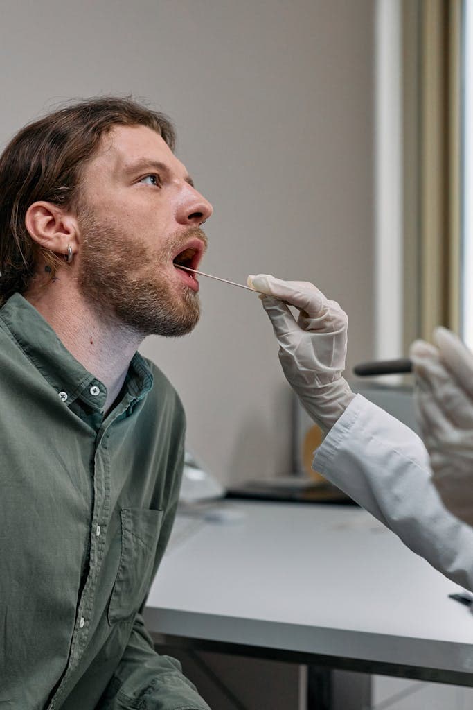 Healthcare worker administering a COVID-19 swab test to a male patient in a doctor's office.